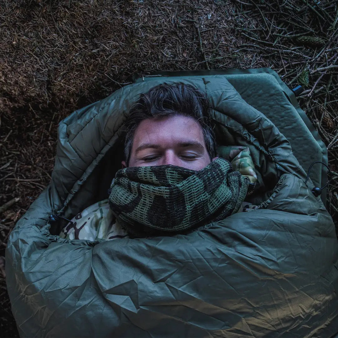 Person sleeping in a green Snugpak sleeping bag under city lights for an exhilarating experience