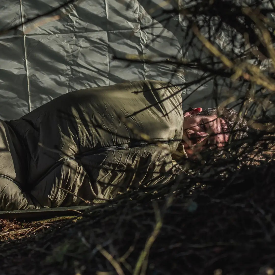 Cozy person inside Snugpak sleeping bag, surrounded by branches and city lights