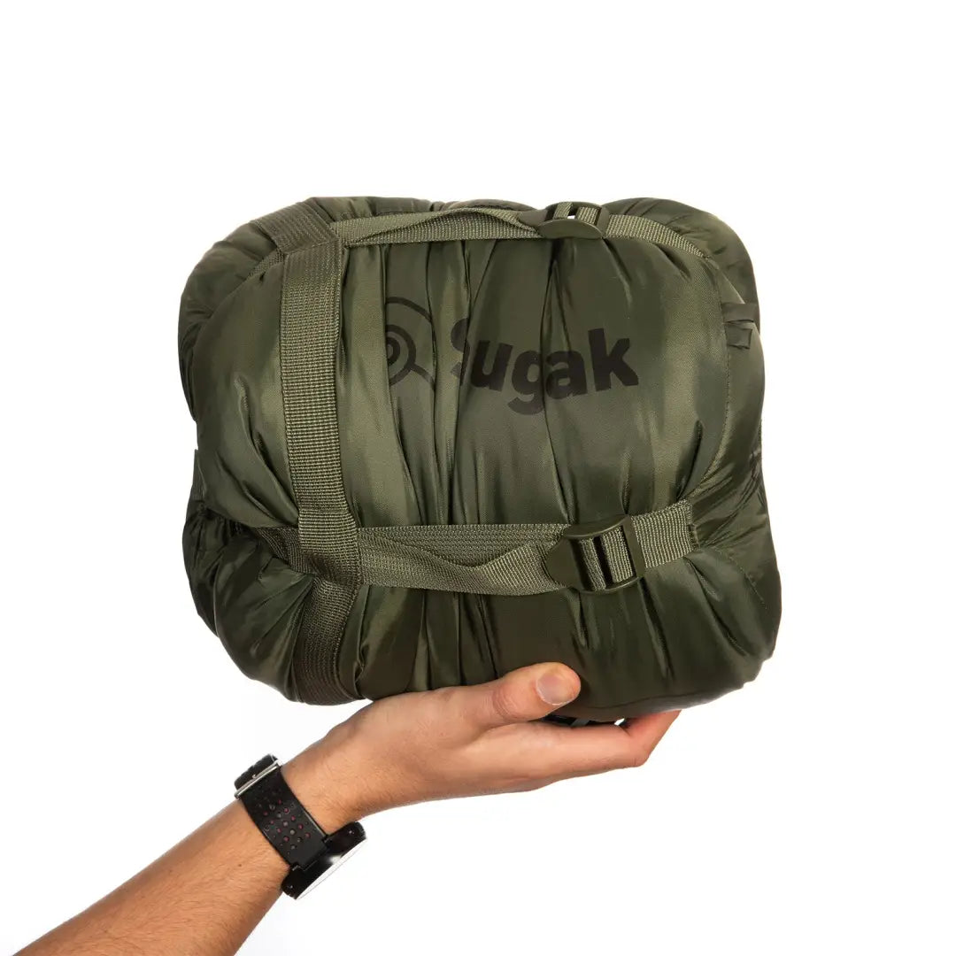 Hand holding an olive green Snugpak sleeping bag, perfect for cozy adventures under city lights