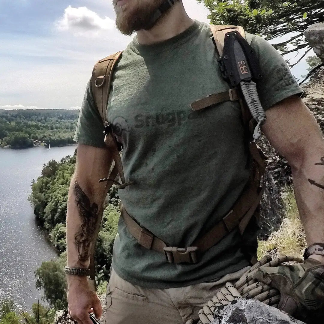 Person in a green Snugpak T-Shirt enjoying the outdoors on a cliff by a lake