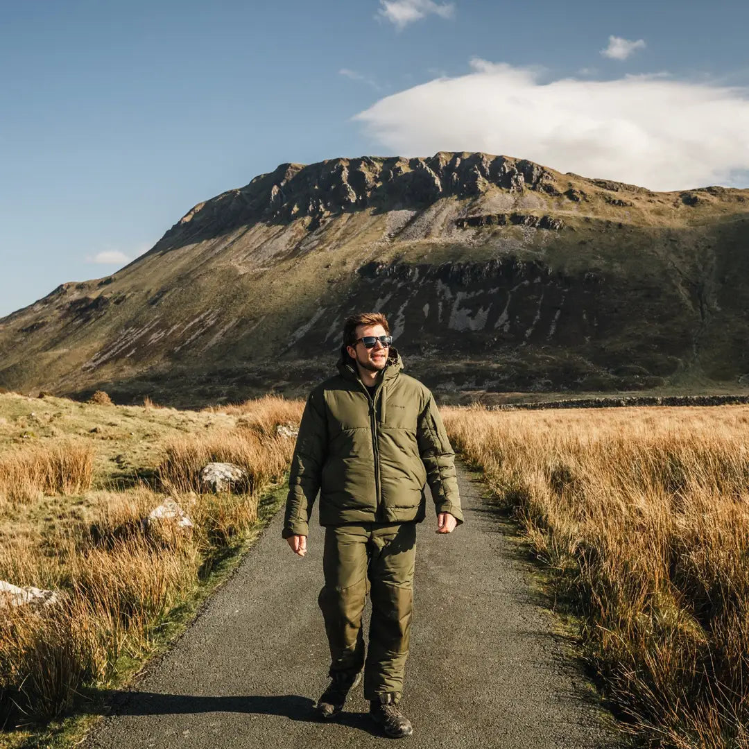 Person walking on a road in a mountainous landscape wearing a Snugpak Tomahawk Cold Jacket