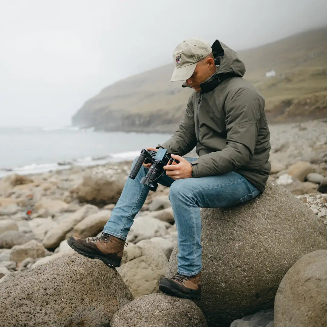 Person on rocky shore wearing a Snugpak Torrent Jacket with binoculars in hand