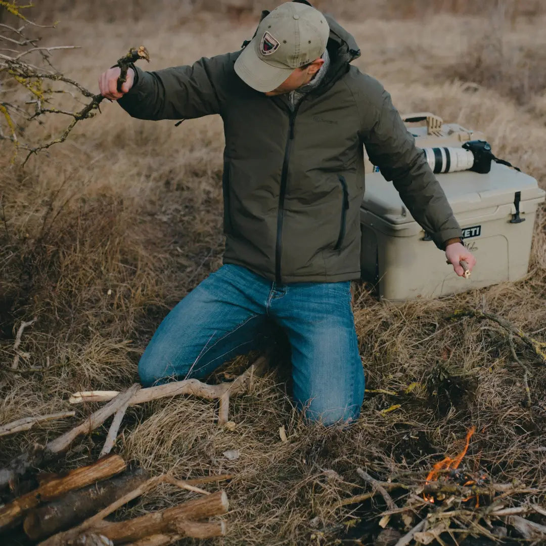 Person in a green Snugpak Torrent Jacket crouching in brush with gear