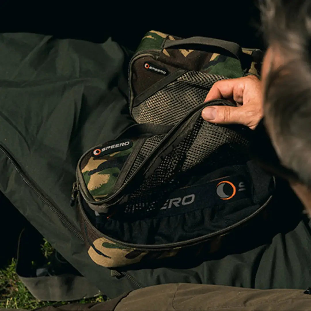 Camouflage motorcycle helmet held above Speero Stash Bag showcasing its stylish design