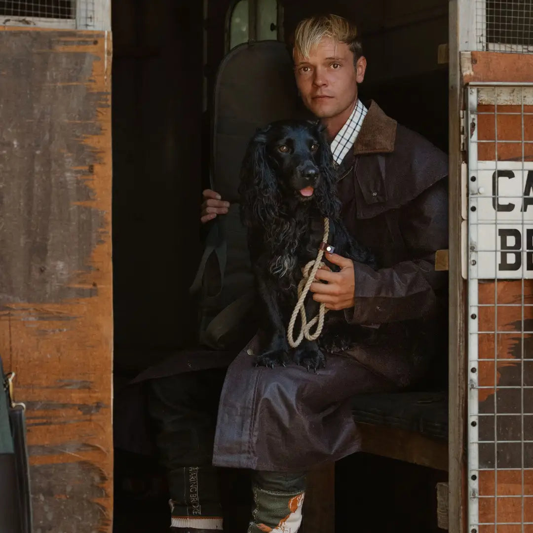 Man in a doorway wearing a Stockman Full Length Wax Coat with a black dog