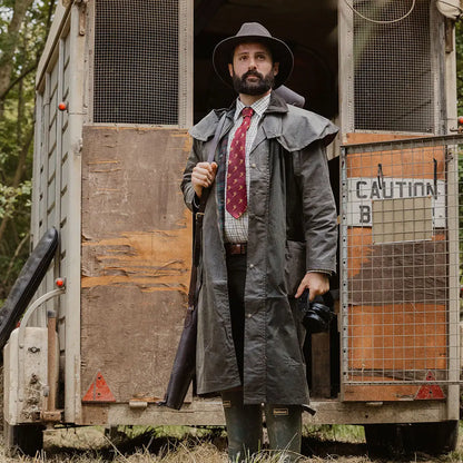 Bearded man in long coat and hat showcases Stockman Full Length Wax Coat by the trailer