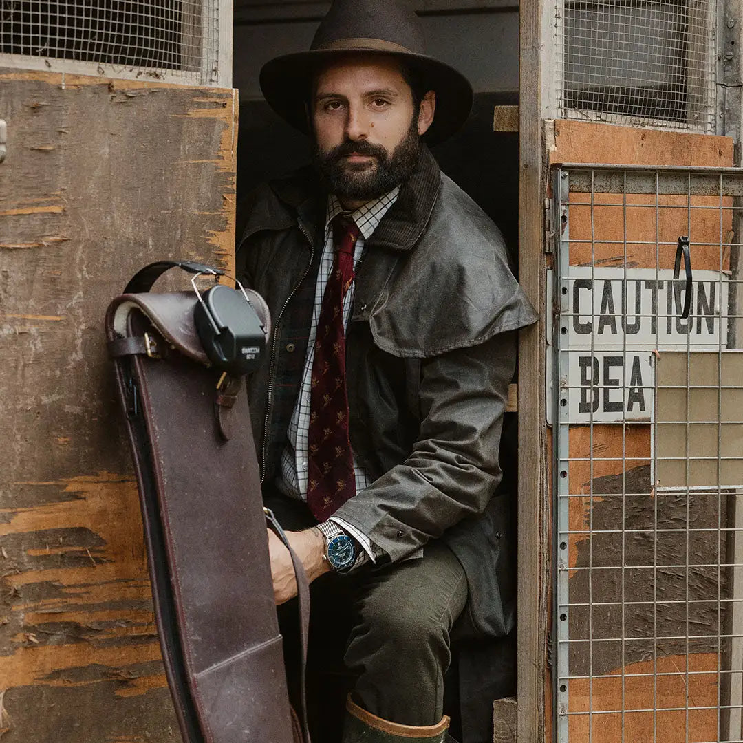 Bearded man in hat and coat with leather case showcasing Stockman Full Length Wax Coat