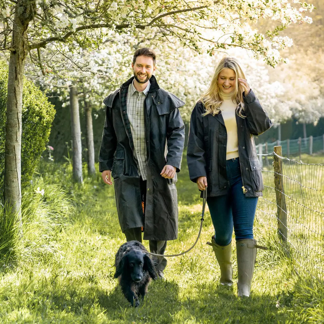 Couple in a Stockman coat walking a black dog under blooming trees