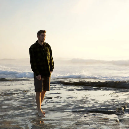 Person in a Ranger Bush Shirt standing ankle-deep in ocean waves at the shoreline