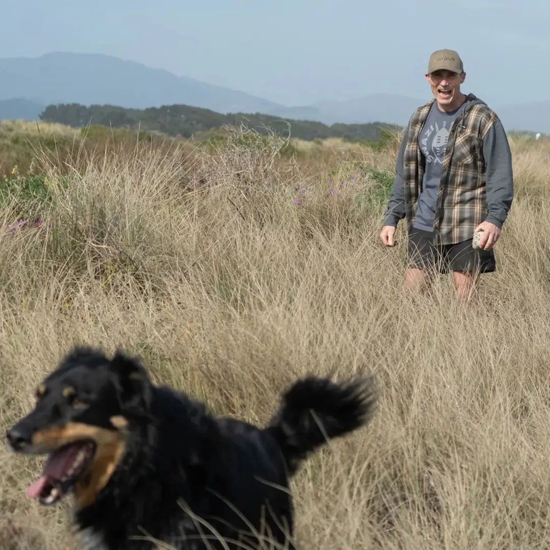 Black dog running through tall grass wearing a Swazi Apprentice Hooded Shirt