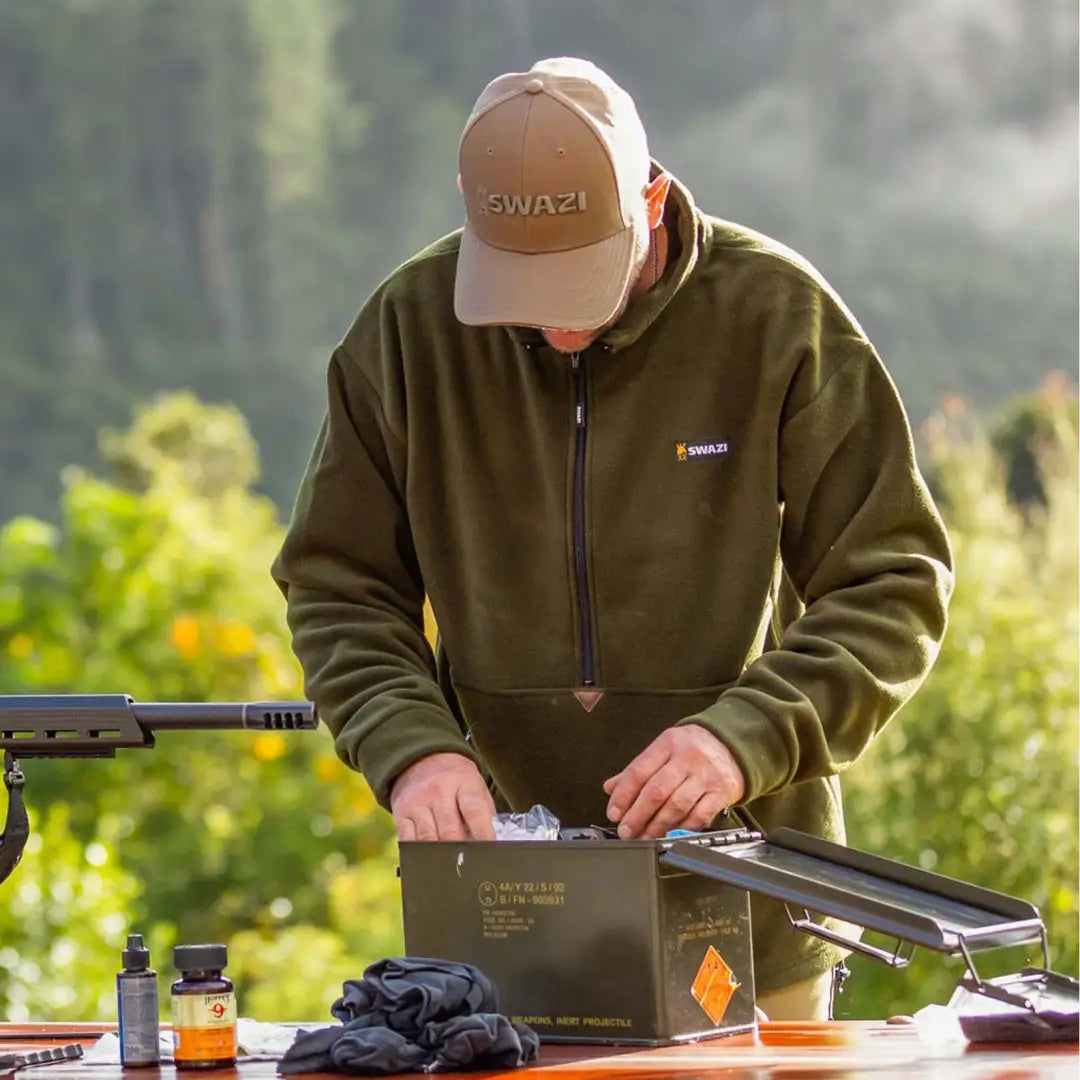 Person in a tan cap and olive doughroaster fleece working outdoors on equipment