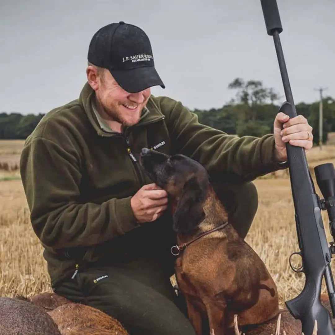 Man in Swazi Doughroaster Fleece petting a dog and holding a rifle outdoors