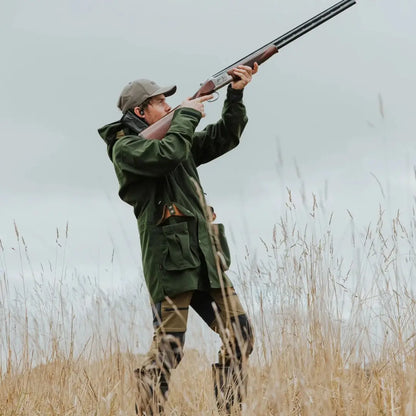 Hunter in camouflage aiming shotgun, showcasing stylish Wapiti coat for outdoors person wanting durability