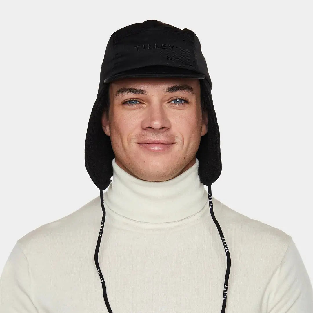 Person in a white turtleneck wears a Tilley Rove Aviator Hat black with ear flaps