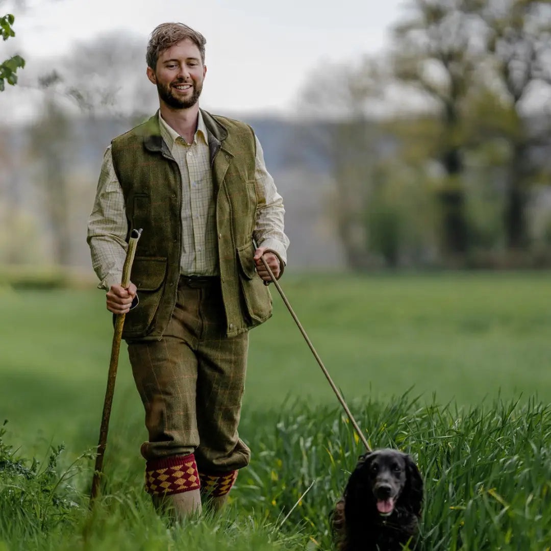 Man in country clothing with a Tweed Gilet walking a black dog on a leash