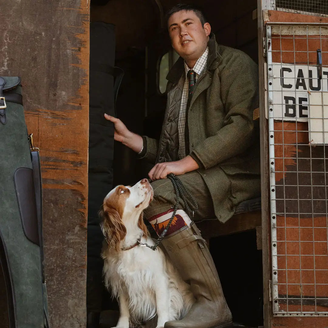 Man in a green suit with a spaniel by his feet, showcasing an English-made tweed shooting jacket