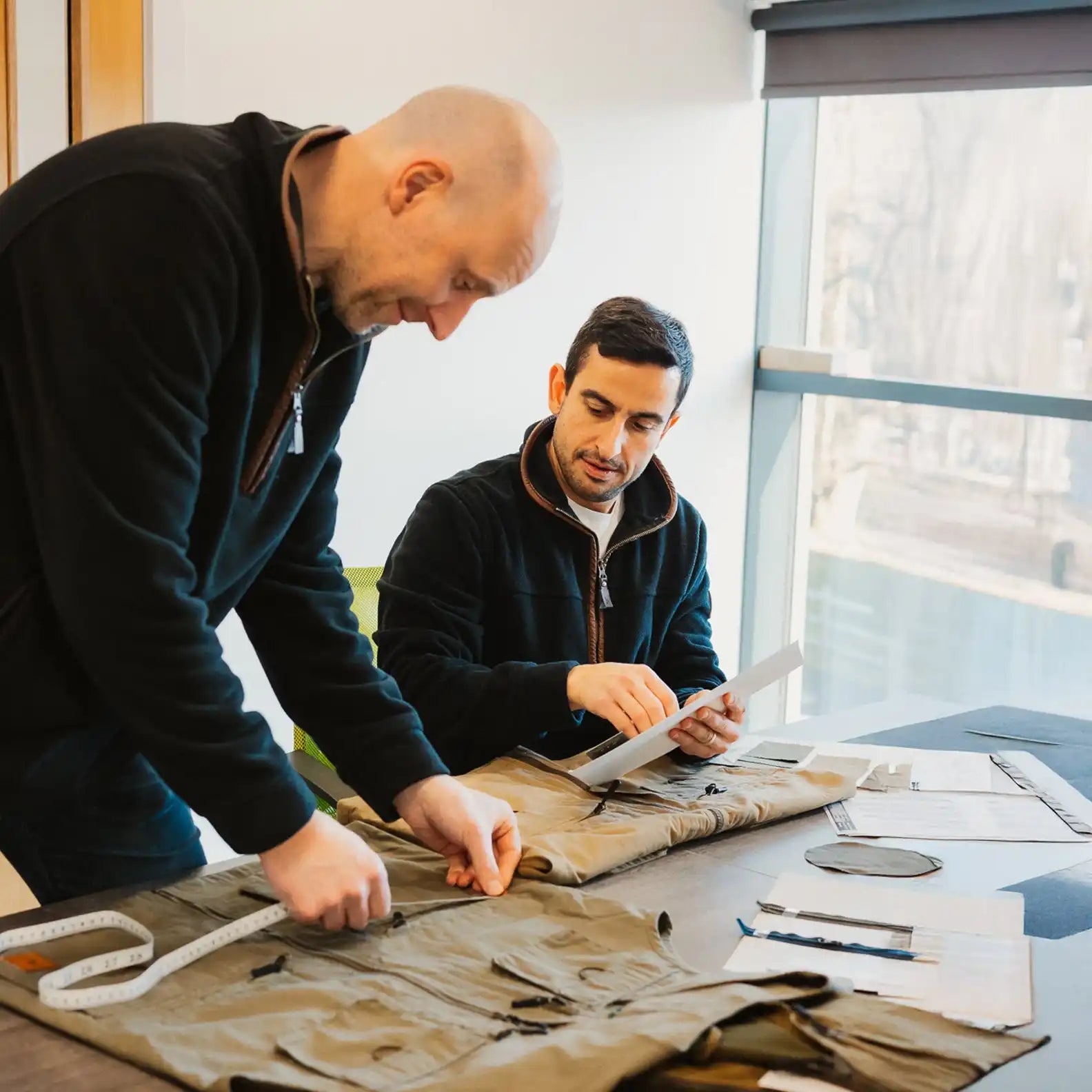 Two men inspecting khaki fabric.