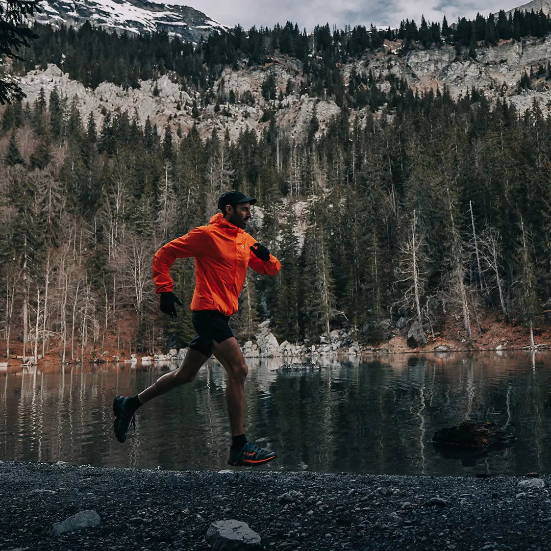 Runner in a bright orange Venture Ultralight Performance Running Jacket by a lake