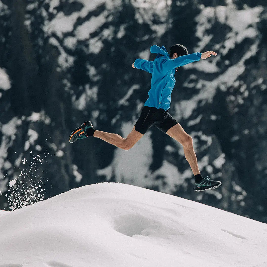 Person in a blue jacket offers waterproofing while joyfully leaping through snow